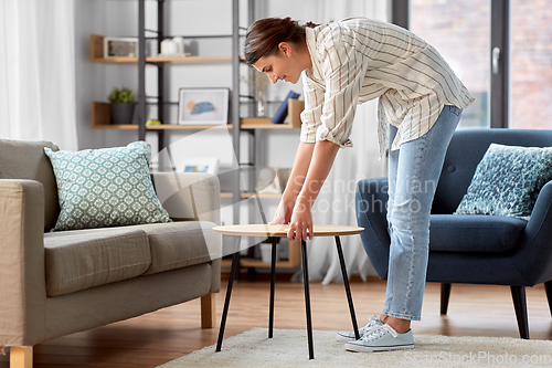 Image of woman placing coffee table next to sofa at home