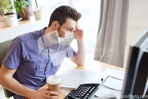 Image of office worker in mask with computer and coffee