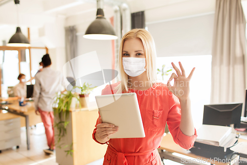 Image of woman in mask with tablet pc showing ok at office