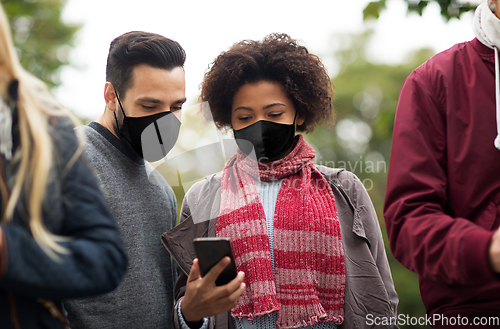 Image of friends in masks with smartphone outdoors