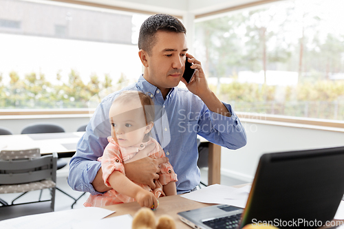 Image of father with baby calling on phone at home office