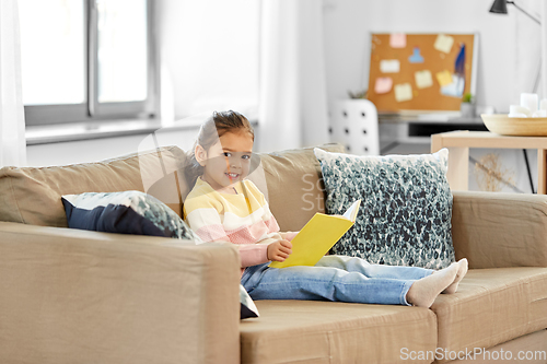 Image of happy smiling little girl reading book at home