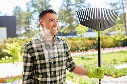 Image of happy middle-aged man with leaf rake at garden