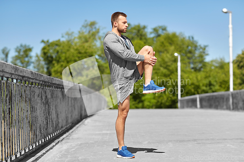 Image of man stretching leg on bridge