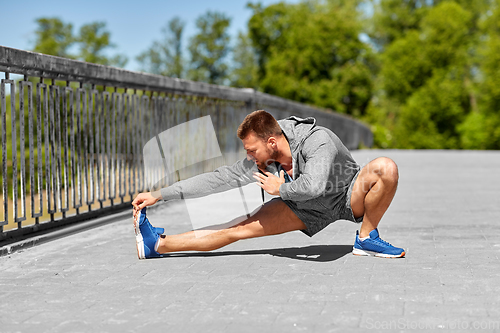 Image of man stretching leg on bridge