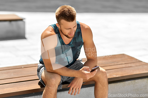 Image of man with smartphone sitting on bench outdoors