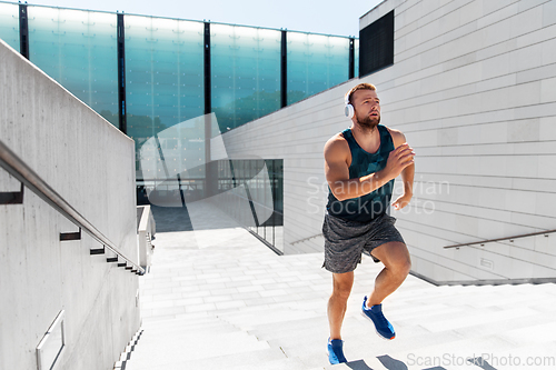 Image of young man in headphones running upstairs outdoors