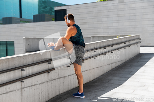 Image of young man in headphones stretching leg outdoors