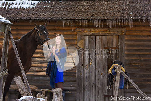 Image of A girl stands with a horse against the background of an old wooden house
