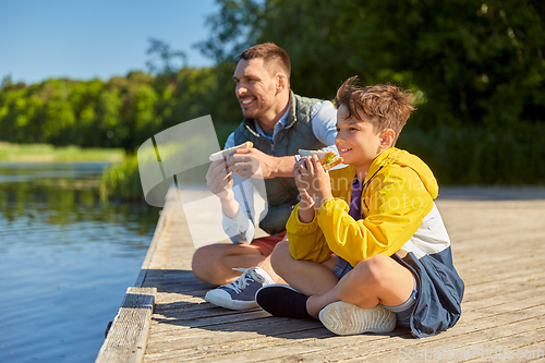 Image of father and son eating sandwiches on river berth