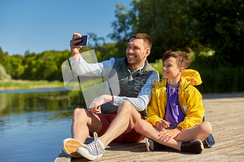 Image of father and son taking selfie with phone on river