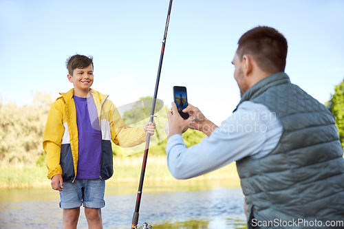 Image of father photographing son with fishing rod on river