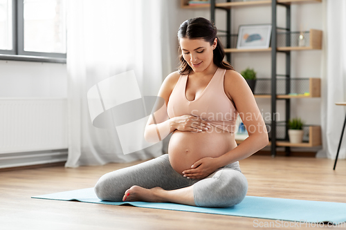 Image of happy pregnant woman sitting on yoga mat at home