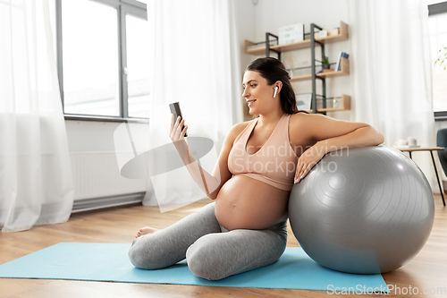 Image of pregnant woman with smartphone and fitball at home