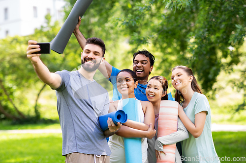 Image of happy people with yoga mats taking selfie at park