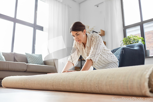 Image of young woman unfolding carpet at home
