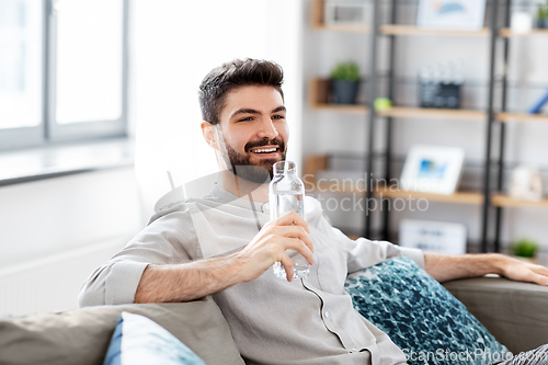 Image of happy man drinking water from glass bottle at home