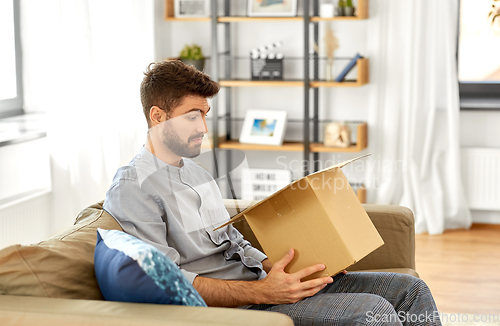 Image of disappointed man opening parcel box at home