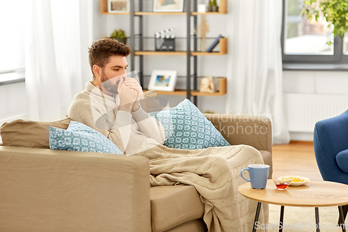 Image of sick young man in blanket with hot tea at home