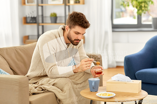 Image of sick young man in blanket drinking hot tea at home