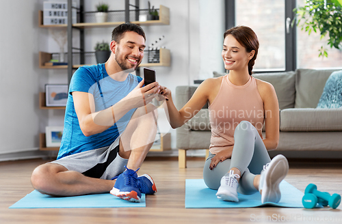 Image of happy couple with smartphone doing sports at home