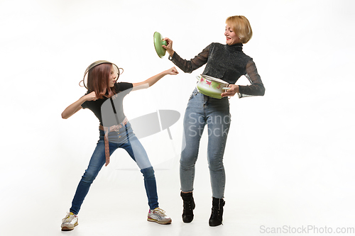 Image of Mom and daughter have fun using kitchen utensils, the girl attacks, mom defends herself with a pot lid