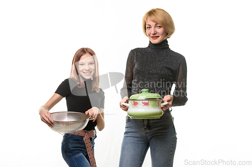 Image of Mom stands with a saucepan, daughter stands with a sieve, both smile and look into the frame