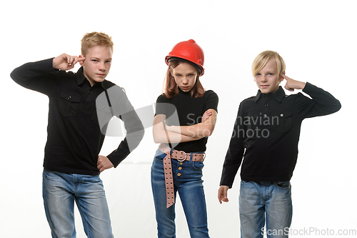 Image of Two boys tease a girl, the girl is standing in a helmet in a helmet and puffed out her cheeks