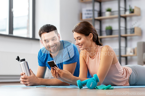 Image of happy couple with smartphone after sports at home