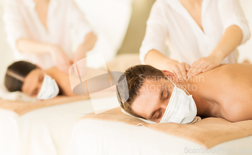 Image of couple in masks having back massage at spa