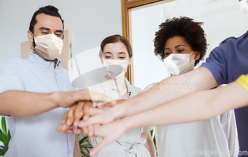 Image of people in masks stacking hands at office