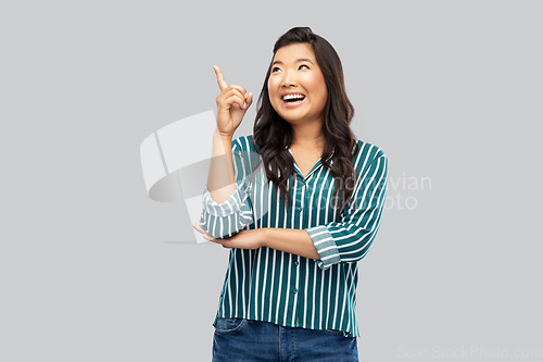 Image of happy asian woman pointing finger up on grey