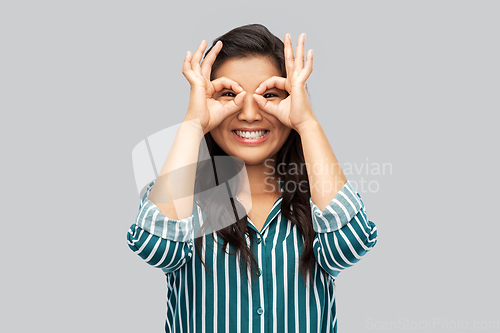 Image of smiling asian woman looking through finger glasses