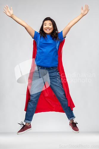 Image of happy asian woman in red superhero cape jumping