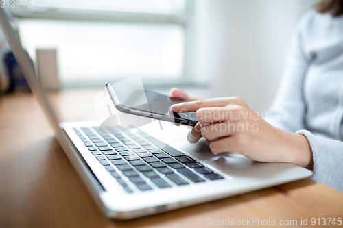 Image of Woman hand typing on laptop keyboard with mobile phone