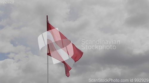 Image of Latvia flag on the flagpole waving in the wind against a blue sky with clouds. Slow motion