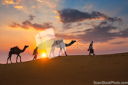 Image of Indian cameleers camel driver with camel silhouettes in dunes on sunset. Jaisalmer, Rajasthan, India