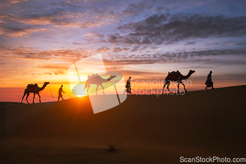 Image of Indian cameleers camel driver with camel silhouettes in dunes on sunset. Jaisalmer, Rajasthan, India