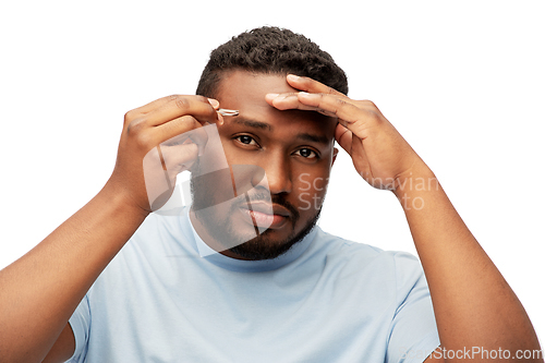 Image of african man with tweezers tweezing his eyebrow