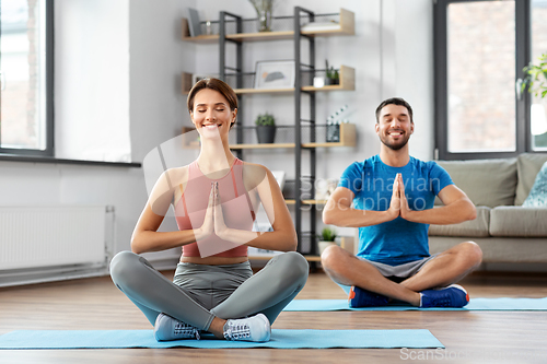 Image of happy couple meditating in yoga lotus pose at home