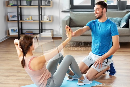 Image of woman with personal trainer doing sit ups at home