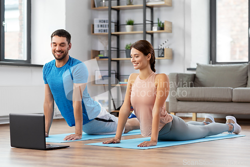 Image of happy couple with laptop exercising at home