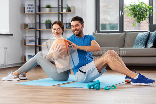 Image of happy couple exercising with ball at home
