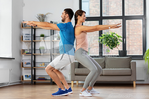 Image of happy couple exercising and doing squats at home