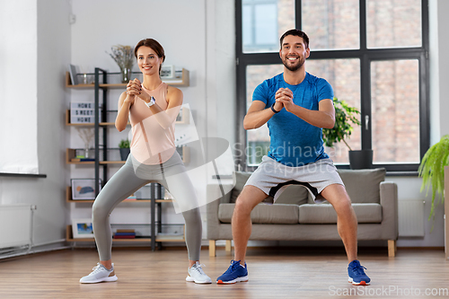 Image of happy couple exercising and doing squats at home