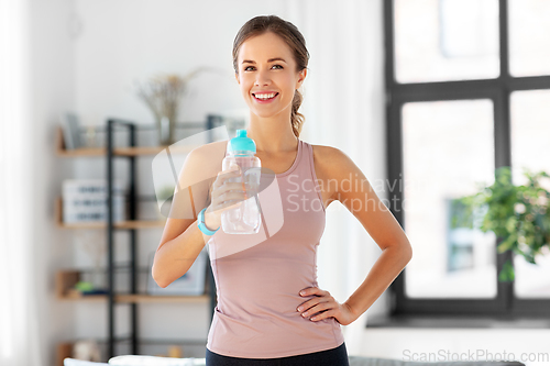 Image of smiling young woman with bottle of water at home
