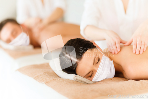 Image of couple in masks having back massage at spa