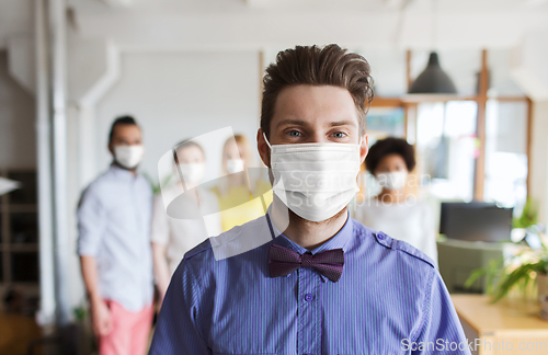 Image of young man in mask over creative team at office