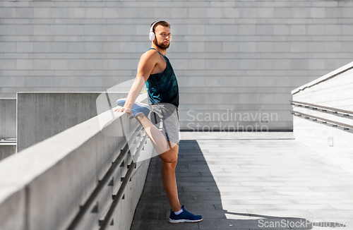 Image of young man in headphones stretching leg outdoors
