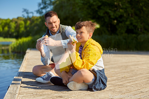 Image of father and son eating sandwiches on river berth